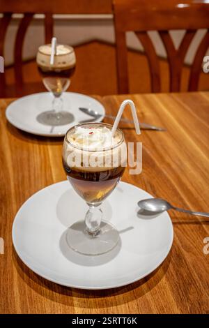 Two glasses of Irish Coffee on two plates placed on a wooden table Stock Photo