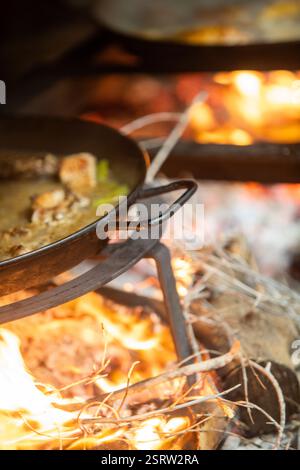 Close-up shot of a traditional wood-fired paella cooker, with flames and embers beneath a paella pan. Stock Photo