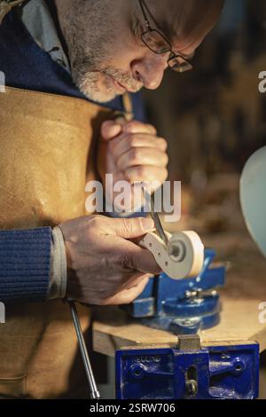 Italian luthier is meticulously carving the scroll of a violin using a chisel, his focused expression reflecting the precision and passion he dedicate Stock Photo