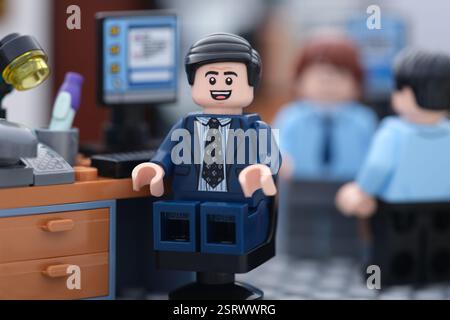 Tambov, Russian Federation - February 16, 2025 A happy Lego businessman minifigure sitting on a chair behind a computer in an office while his colleag Stock Photo