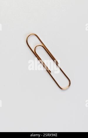 paper clips made of metal for the systematization of documents and paper, large sized copper paper clips lie on white blank paper Stock Photo