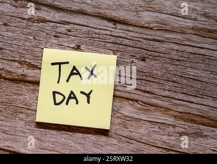 A yellow sticky note with the words tax day written in black sits on a rustic wooden surface. This serves as a reminder of the importance of filing ta Stock Photo