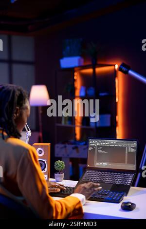 Computer scientist writes code on laptop screen while in apartment office using Java programming languages. African american teenager remotely working on fixing database errors Stock Photo