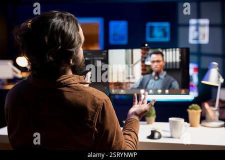 Focus on cybersecurity specialist helped by african american coworker in blurry background on computer monitor during internet videocall meeting to look for company security vulnerabilities Stock Photo