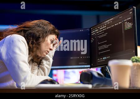 Tired woman hurting from too much stress accumulated while doing software quality assurance, reading source code on computer. Engineer suffers from headache after inspecting coding on PC for too long Stock Photo