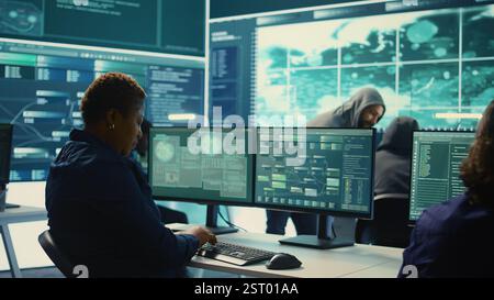 Governmental hackers analyzing big data for cyber threat detection, working at agency desks. Professional expert woman analyzes cyber intelligence and prevention of digital threats. Camera B. Stock Photo