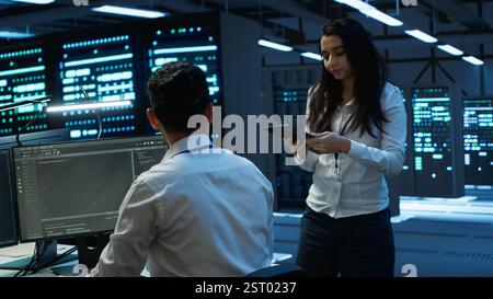 Coworkers in high tech data center monitoring security threats, implementing cybersecurity measures. IT staff members ensuring compliance with server room workspace regulations Stock Photo