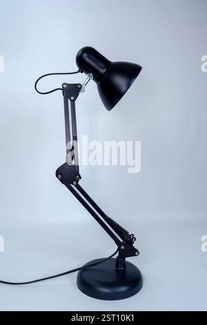 Black metal desk lamp with an adjustable articulated arm and round base, isolated on a white background. Modern and functional lighting for workspace Stock Photo