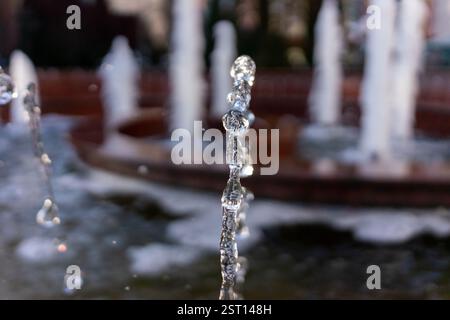 Water droplets shoot upward from a bustling fountain in a city park, sparkling in sunlight. The rhythmic flow of water attracts onlookers, creating a Stock Photo