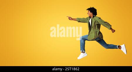 Look There. Overjoyed black guy pointing aside while jumping up in air Stock Photo