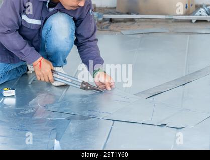 The worker uses shears to cut the metal sheet along the marked lines to fold it into the desired shape. Stock Photo