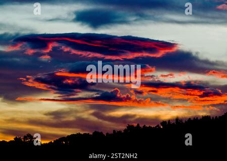 Red clouds drift like fire across the sky, whispering secrets of the sun’s final sigh. Stock Photo