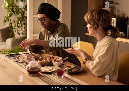 Two people sitting at dining table, savoring an array of Asian dishes under warm indoor lighting, engaging in relaxed dinner conversation Stock Photo