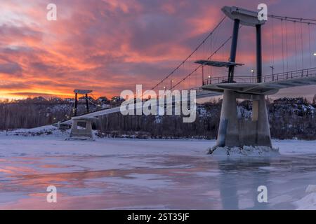 Fort Edmonton Footbridge at sunset in winter season with red color in sky and reflection on the river ice Stock Photo