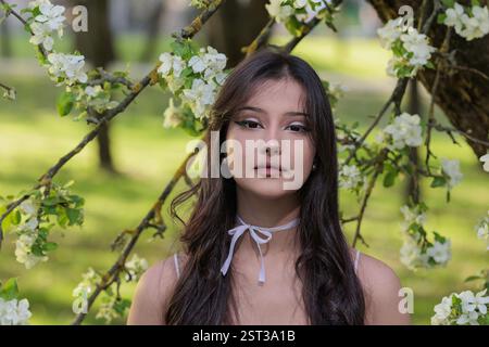 Beautiful Girl with long hair poses near white blossoming apple trees Stock Photo