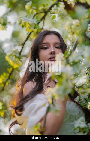 Beautiful Girl with long hair poses near white blossoming apple trees Stock Photo