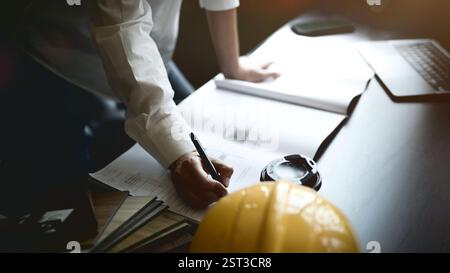 A professional female interior designer or architect leans over her desk in the office, working on a new project, reviewing a blueprint. Stock Photo