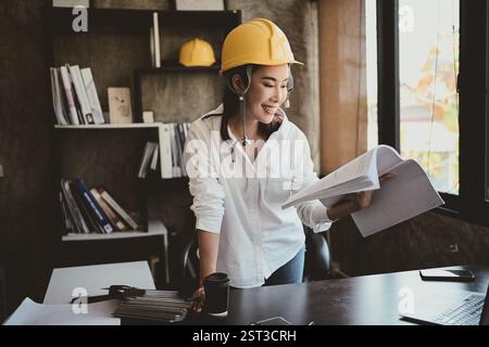 A professional, confident Asian female architect or engineer is reviewing documents at her desk in the office. Stock Photo
