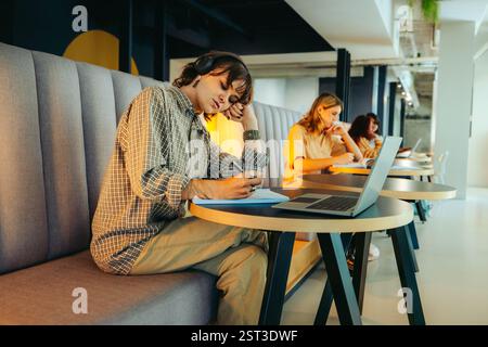 Young students are diligently preparing for exams in a bright, modern study space, using laptops and notebooks to focus on learning and concentration. Stock Photo