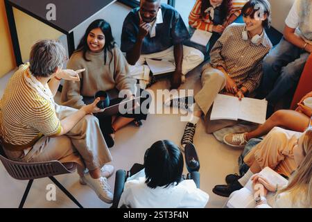 Teacher engaging with students in a casual classroom setting, promoting open discussion and collaboration among a diverse group sitting on the floor. Stock Photo