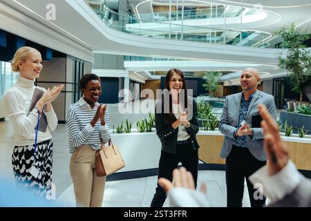 A diverse corporate team claps and smiles in a modern, open office space, celebrating their recent success. The multiethnic group exudes a sense of ac Stock Photo