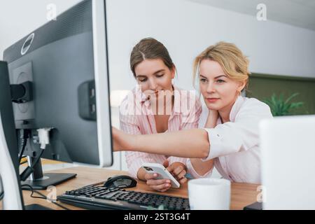 Two female stock brokers in formal wear is working in the office by pc. Stock Photo