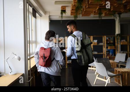 Rear view of young man with Down syndrome and his teacher talking while walking down the school hallway. Stock Photo