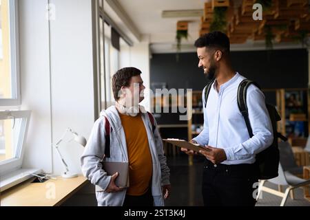 Young man with Down syndrome and his teacher talking while walking down the school hallway. Stock Photo