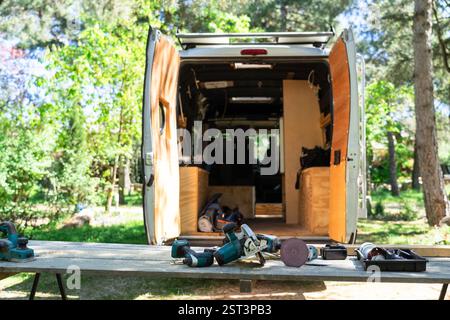 Power tools lying on a wooden table in front of a van converted into a mobile workshop, parked in nature Stock Photo
