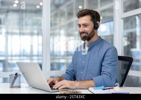 Man with headset working inside office with laptop, using video call for online communication remotely. Support service worker, and assistance at workplace. Stock Photo