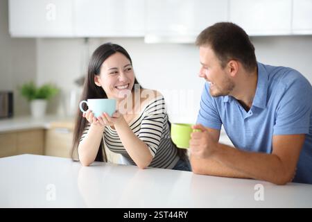 Interracial friends drinking and talking in a kitchen at home Stock Photo