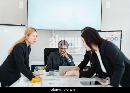 Multicultural business team analyzing data and discussing strategies during a tense meeting, emphasizing teamwork and problem-solving. Stock Photo