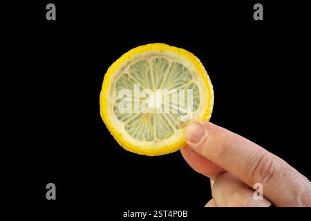 A man's hand holds a yellow slice of lemon on a black background Stock Photo