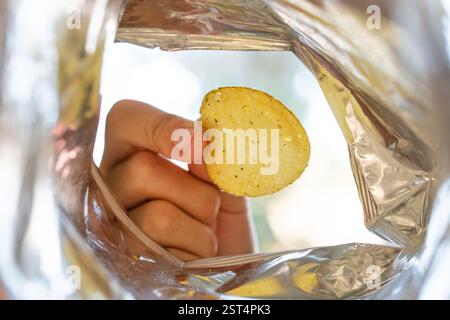 Hand picking potato chips inside snack bag. An open pack of chips. inside pack view Stock Photo