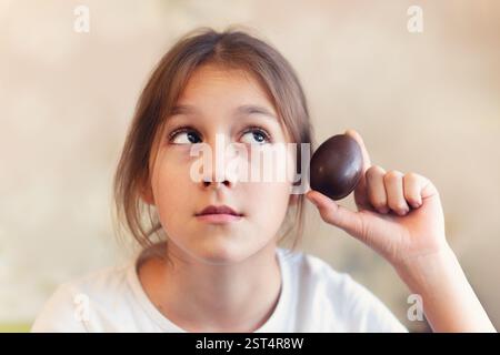 A child opens a chocolate egg. The girl is surprised by the surprise. The girl shakes a chocolate egg while checking the toy. Stock Photo