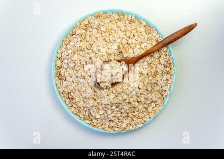 Dry oatmeal in a blue plate and wooden spoon on a white background. Top view. Copy, empty space Stock Photo