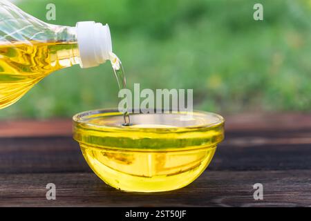 Pouring cooking oil from jug into bowl on wooden table. pouring oil from a bottle into a glass bowl on a wooden table. the process of cooking food. Stock Photo
