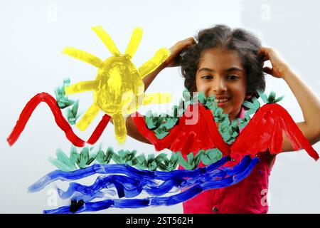 South Asian Indian eight year old girl child wearing red dress with shot hair painting with yellow, red, green, blue color on glass Stock Photo