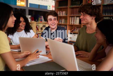 Group of students gathered in the library to work together on a school project, using laptops. Stock Photo