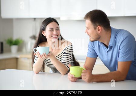 Interracial couple talking and drinking in the kitchen at home Stock Photo