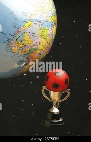 Small metal cup with red and black rubber ball of soccer or football sport and world globe against starry black background depicting world cup footbal Stock Photo