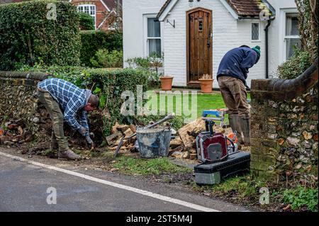 Workmen rebuilding a brick and flint wall reusing old bricks. Stock Photo