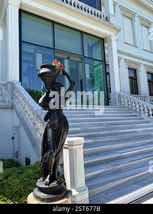 This elegant photograph features a black statue of a woman gracefully holding a decorative vase adorned with flowers, positioned at the base of a gran Stock Photo
