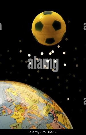 Small yellow and blue rubber ball of soccer or football sport and world globe against a starry black background Stock Photo