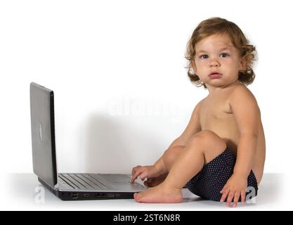 Baby girl sits on the floor with laptop on white background Stock Photo