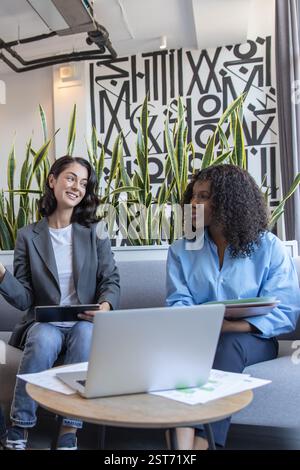Two creative diverse colleagues sitting on sofa in office collaborating on project Stock Photo