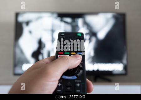 Men with the remote control front of the television. Hand with remote control directed on the TV. A man is relaxing and watching sports on TV. Stock Photo