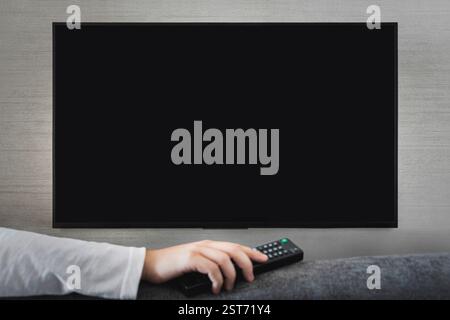 Television remote control changes channels thumb on the black TV screen. selective focus on the off button Stock Photo
