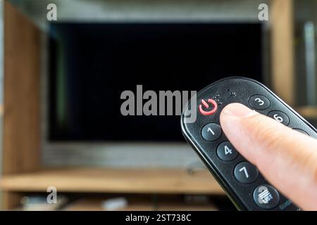 Hand holding remote control for turn off TV. an empty black TV screen. Stock Photo