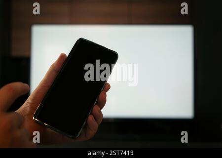Relaxed man with smartphone connected to a tv. Blank screen screen. The form for information. TV screen without information and content. Using a smart Stock Photo